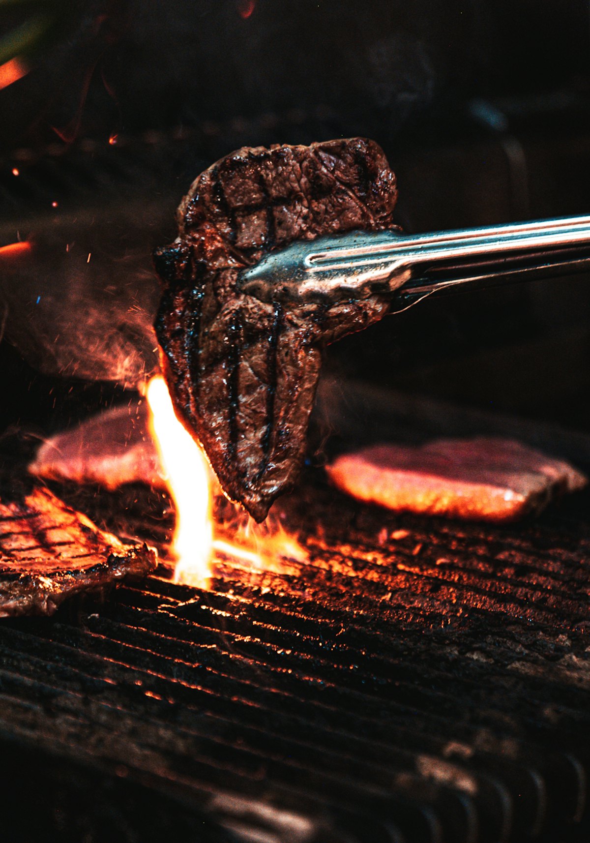 Bife levantado con pinza sobre las brasas