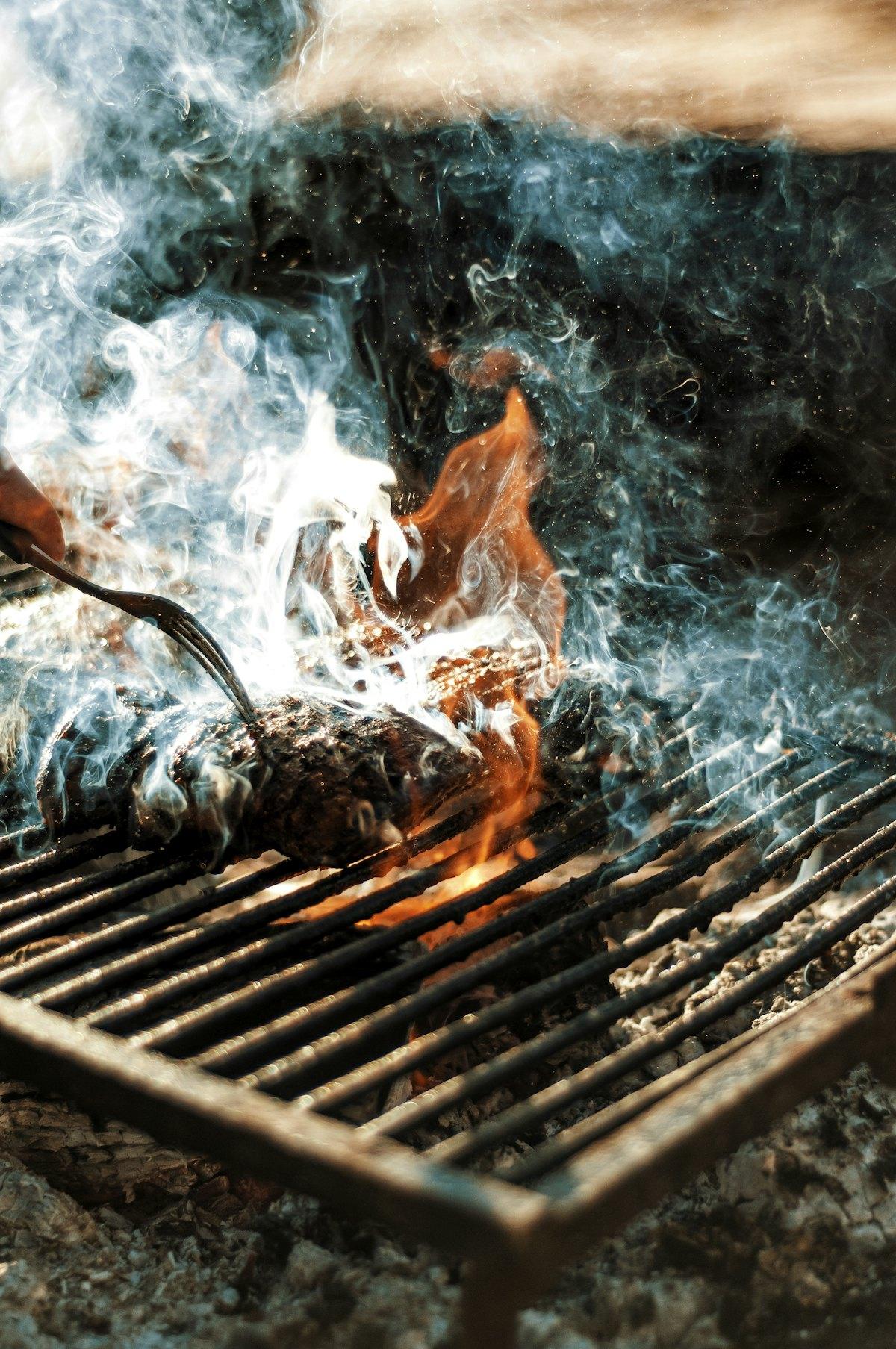 Parrillero dando vuelta la carne entre el humo